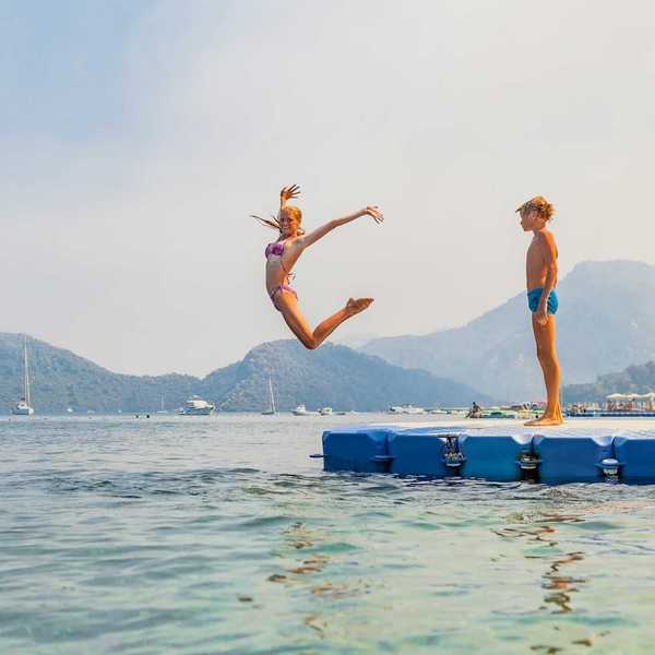 Girl striking a mid-air pose while jumping into water - boy stands and waits his turn
