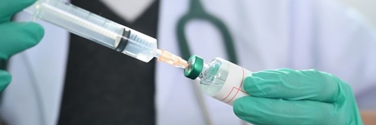 Gloved hands holding a syringe and a vial of vaccine solution