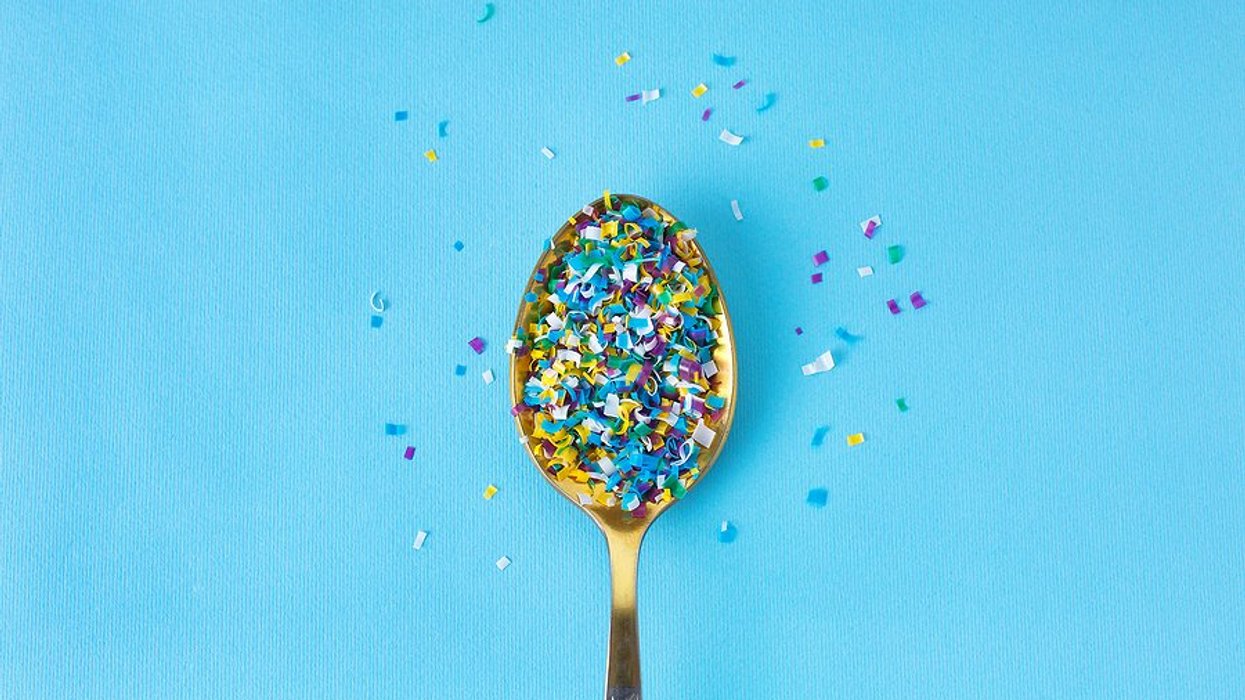 Gold spoon on blue background with tiny pieces of plastic