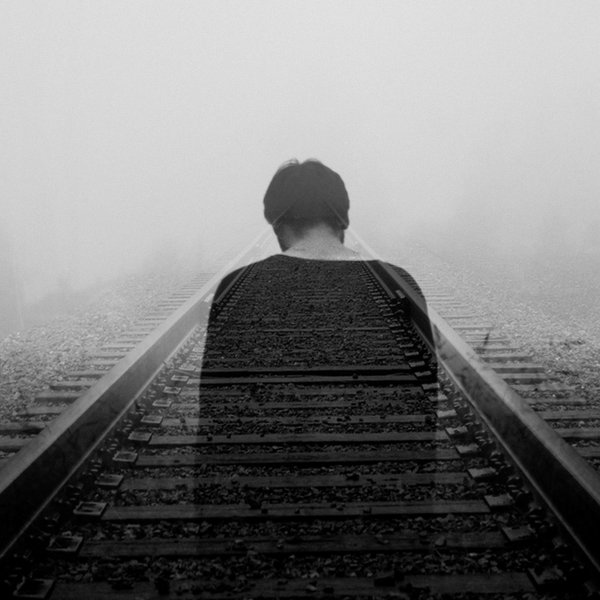 grayscale photo of man wearing black shirt facing a railway