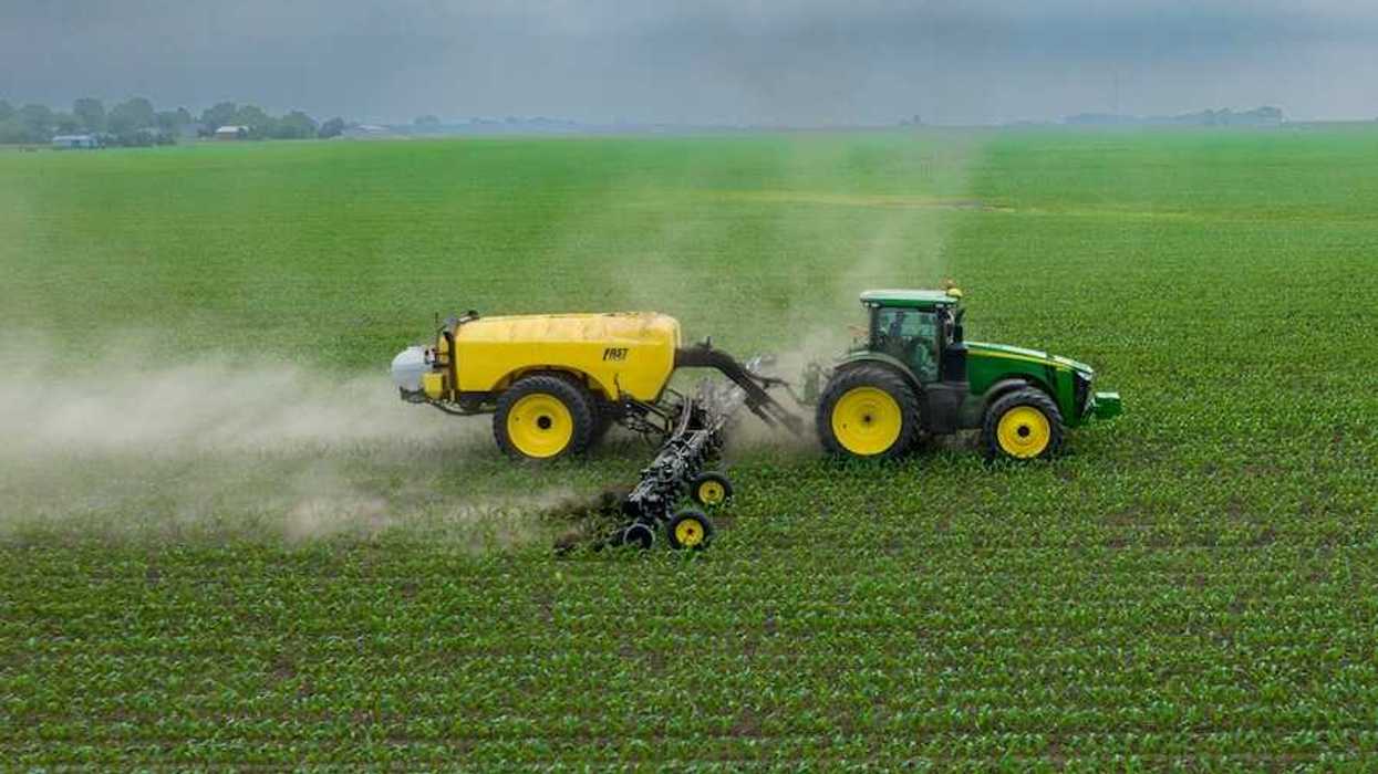 Green and yellow tractor towing a yellow piece of equipment that spreads chemical fertilizer