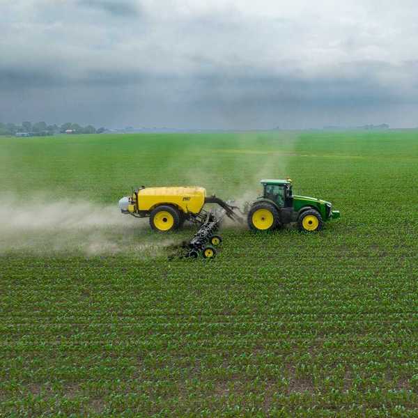 Green and yellow tractor towing a yellow piece of equipment that spreads chemical fertilizer