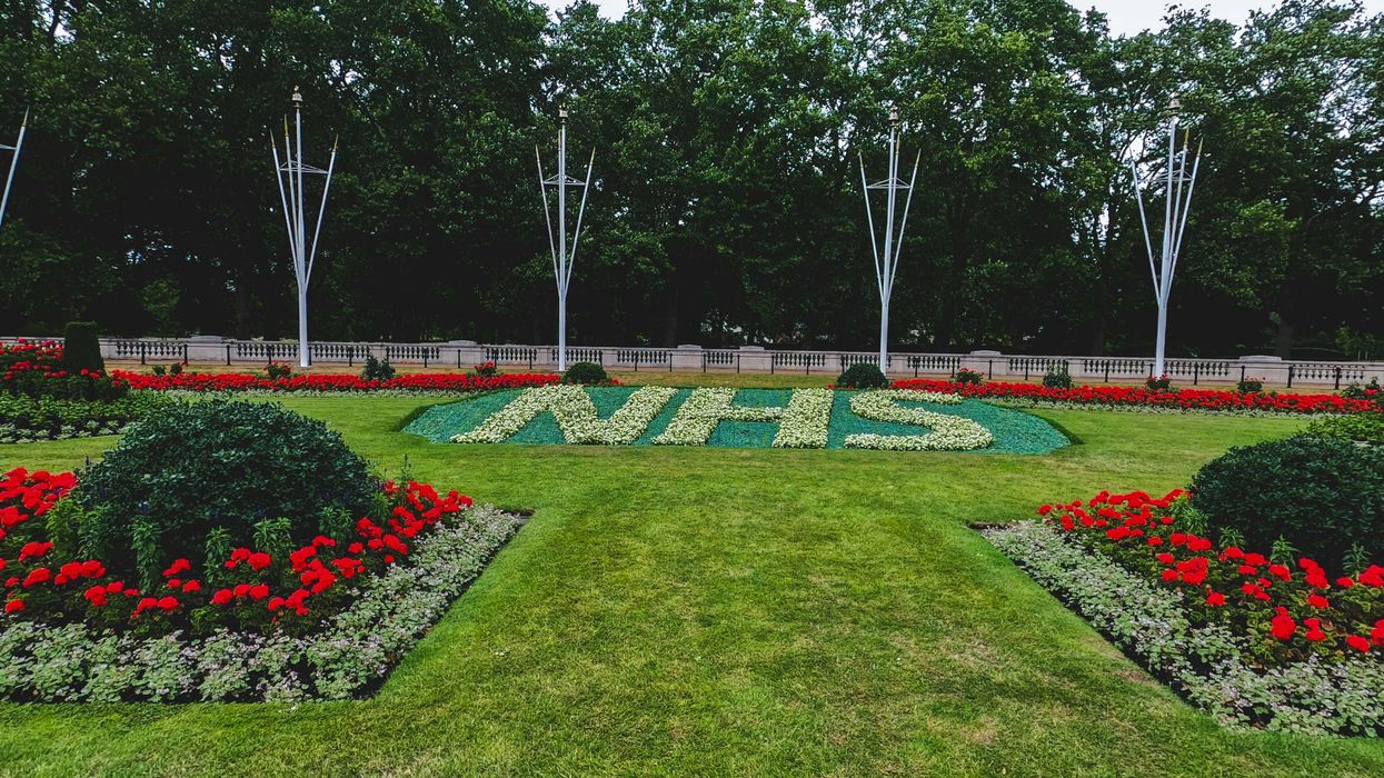 green grass field with trees and red flowers and plants spelling out NHS.