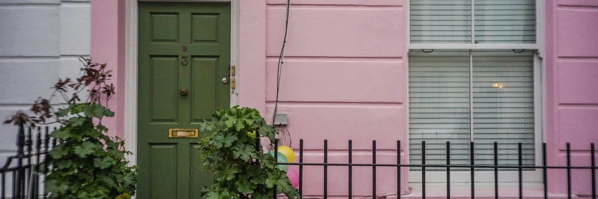 green leafed plants on the stoop next to a pink townhouse with a green door.