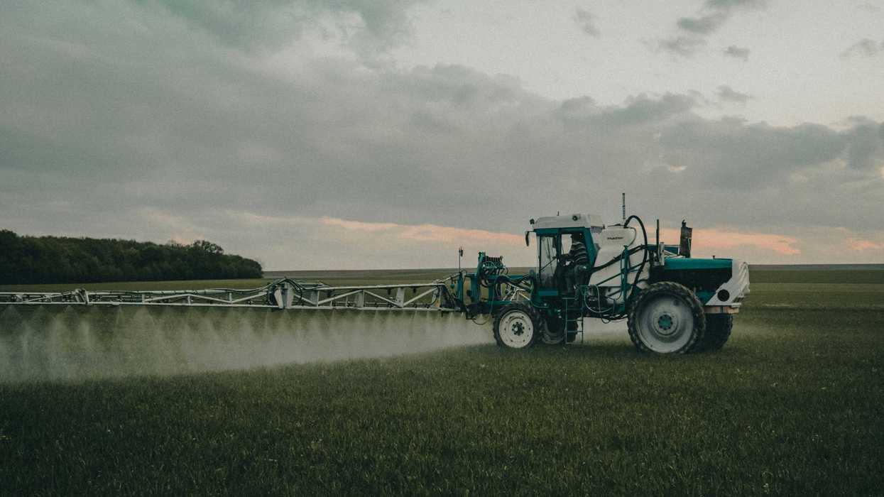 green tractor spraying pesticides on green grass field under cloudy sky during cloudy daytime.