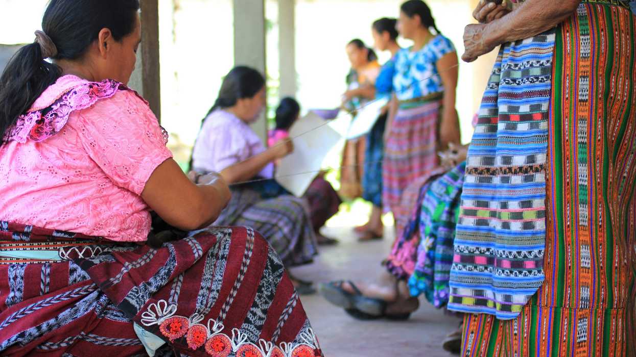 Guatemalan women in colorful dress sitting on floor and standing.