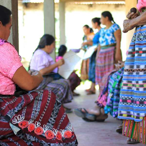 Guatemalan women in colorful dress sitting on floor and standing.