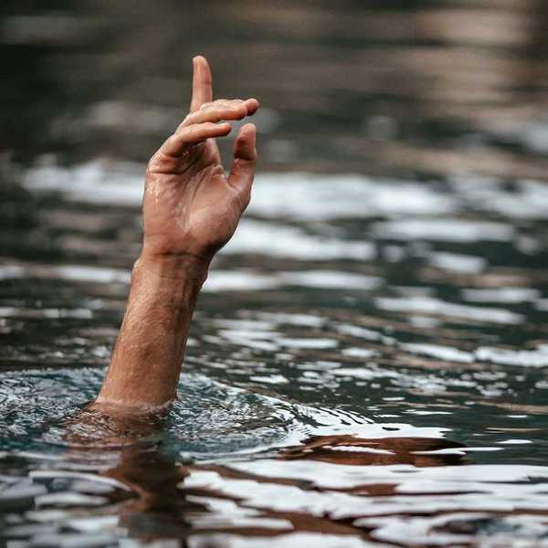Hand and partially submerged forearm sticking out of floodwaters, one finger pointing up