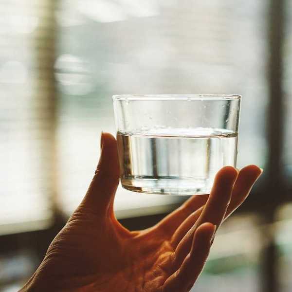 Hand holding a glass of water up to the light