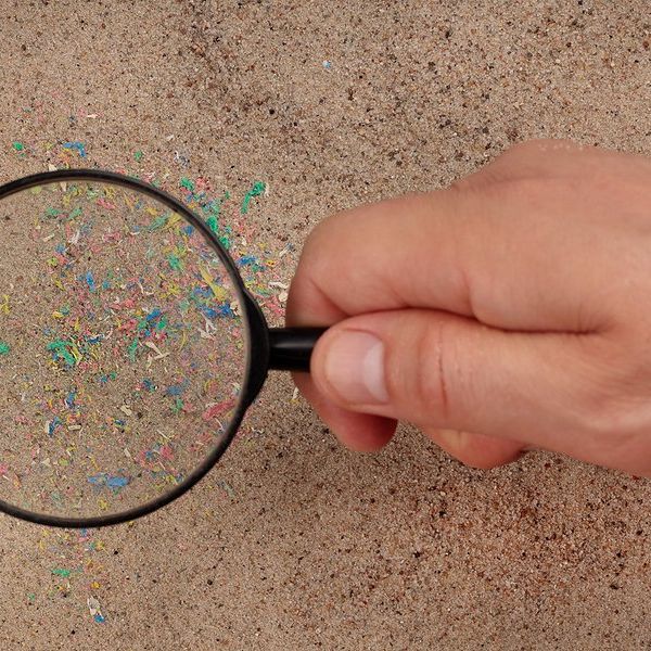 Hand holding a magnifying glass on a beach showing tiny particles of plastic in the sand