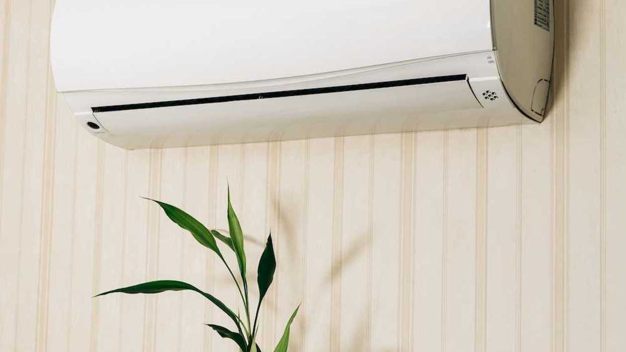Hand holding a remote control directed at a wall-mounted mini-split heating unit