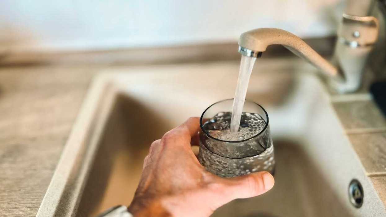 hand holding glass under a running faucet, filling glass with tap water