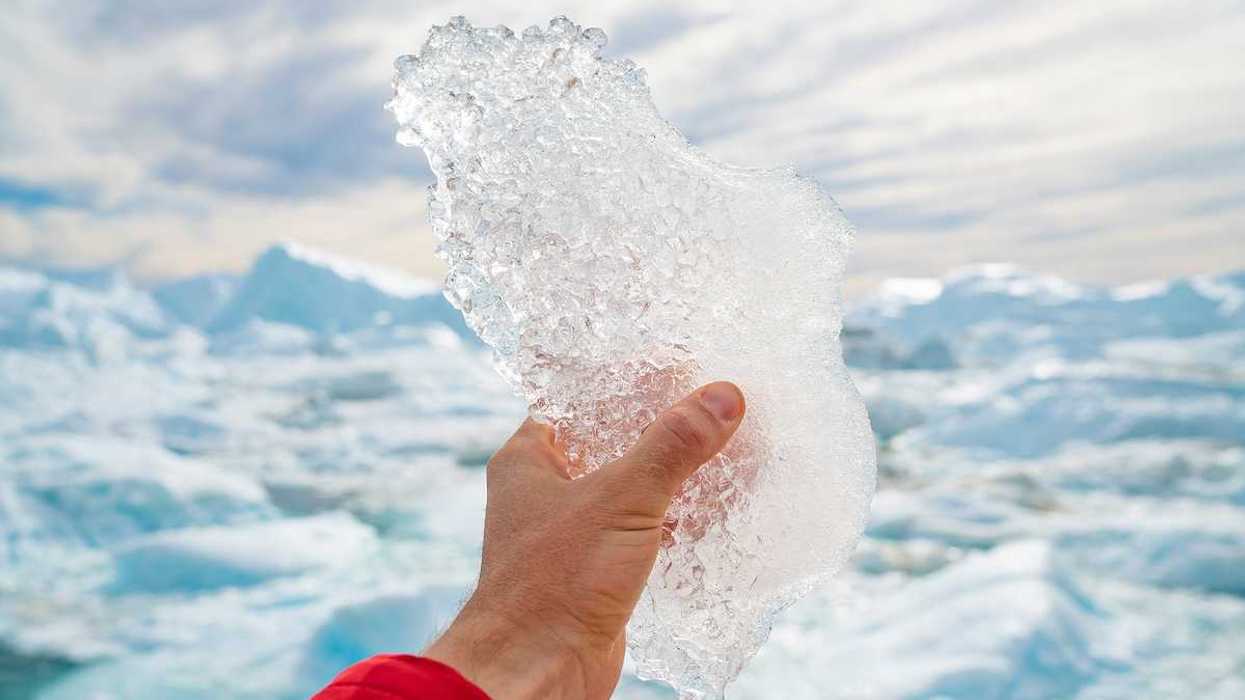 Hand holding melting ice by giant iceberg in Ilulissat icefjord on Greenland.
