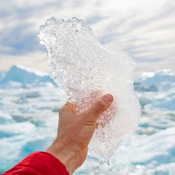 Hand holding melting ice by giant iceberg in Ilulissat icefjord on Greenland.