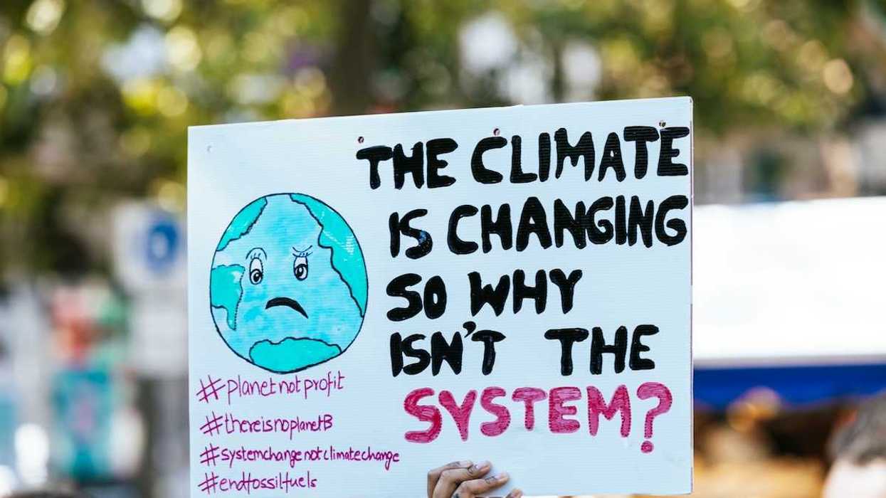 Hand holding sign: "THE CLIMATE IS CHANGING SO WHY ISN'T THE SYSTEM?"