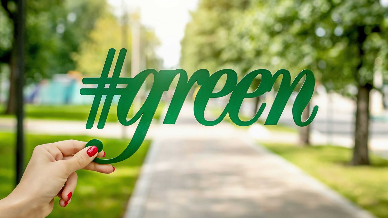 hand holding signage that reads "#green" against a backdrop of trees and grass.