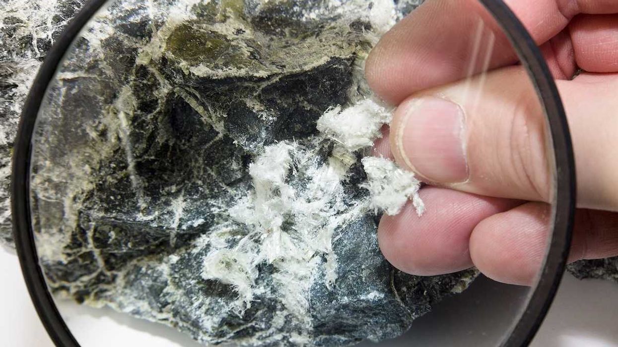 Hand with magnifying glass examines asbestos fibers in stone.