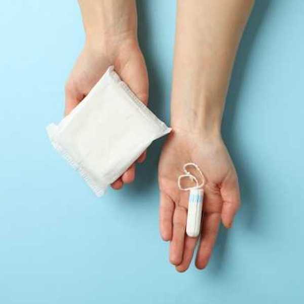 Hands holding a menstrual pad and tampon against a light blue background