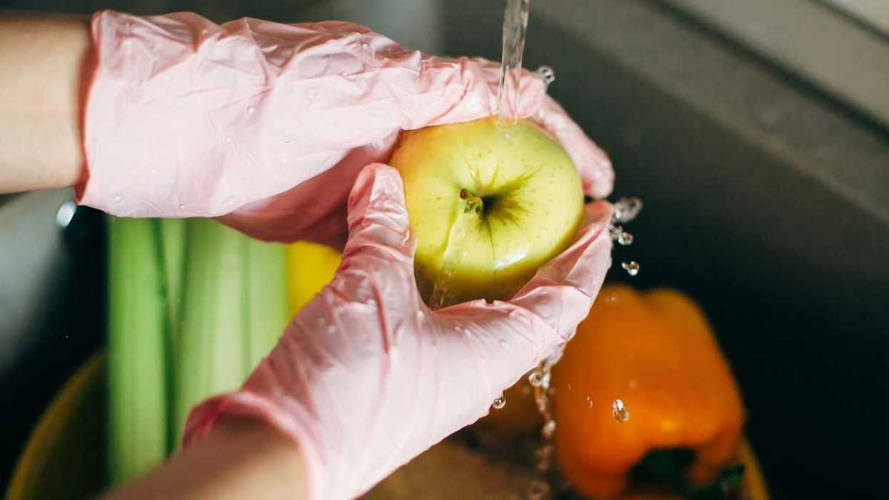 Hands in pink plastic gloves washing an apple under tap water
