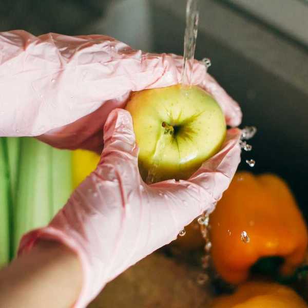 Hands in pink plastic gloves washing an apple under tap water