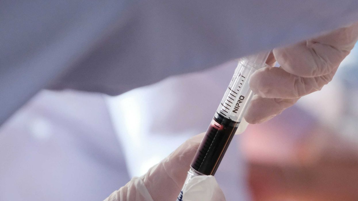hands in white plastic gloves hold a syringe filled with blood.