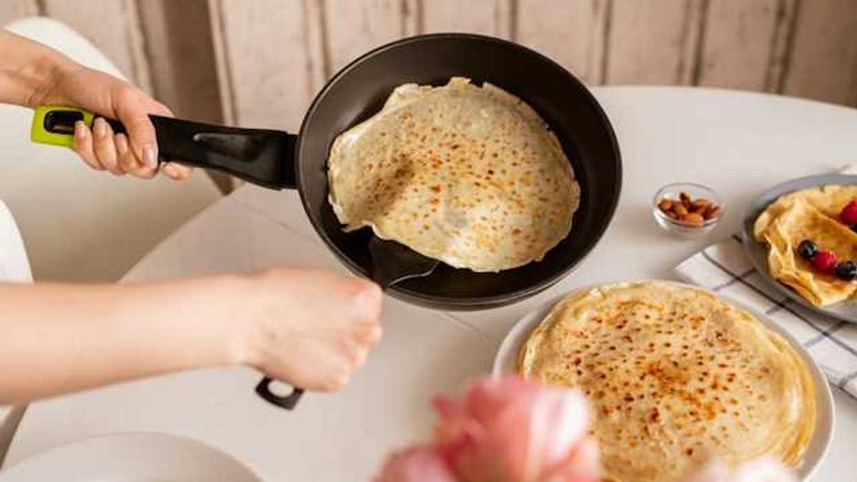 Hands of woman taking out a crepe from a pan to put onto a plate