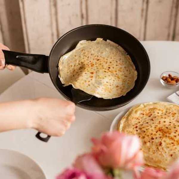 Hands of woman taking out a crepe from a pan to put onto a plate
