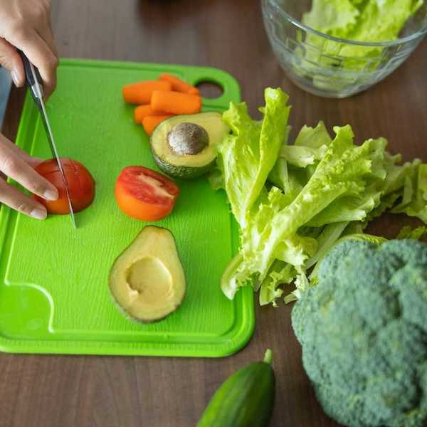 Hands slicing veggies on a plastic cutting board