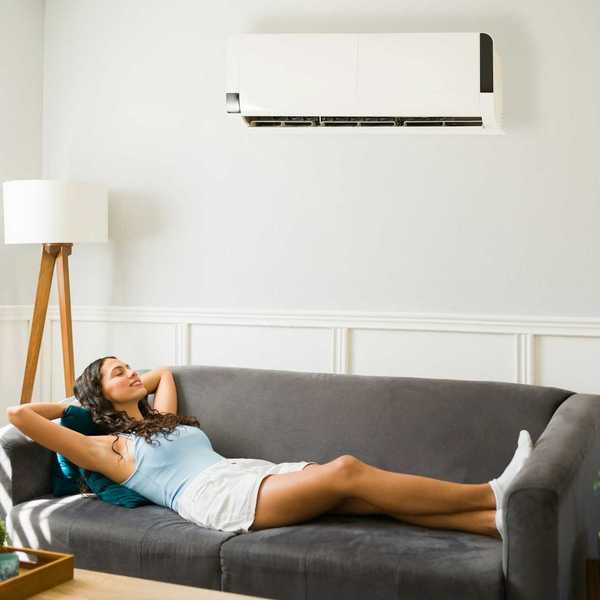 Happy woman relaxing in cool comfort underneath a mini-split heat pump