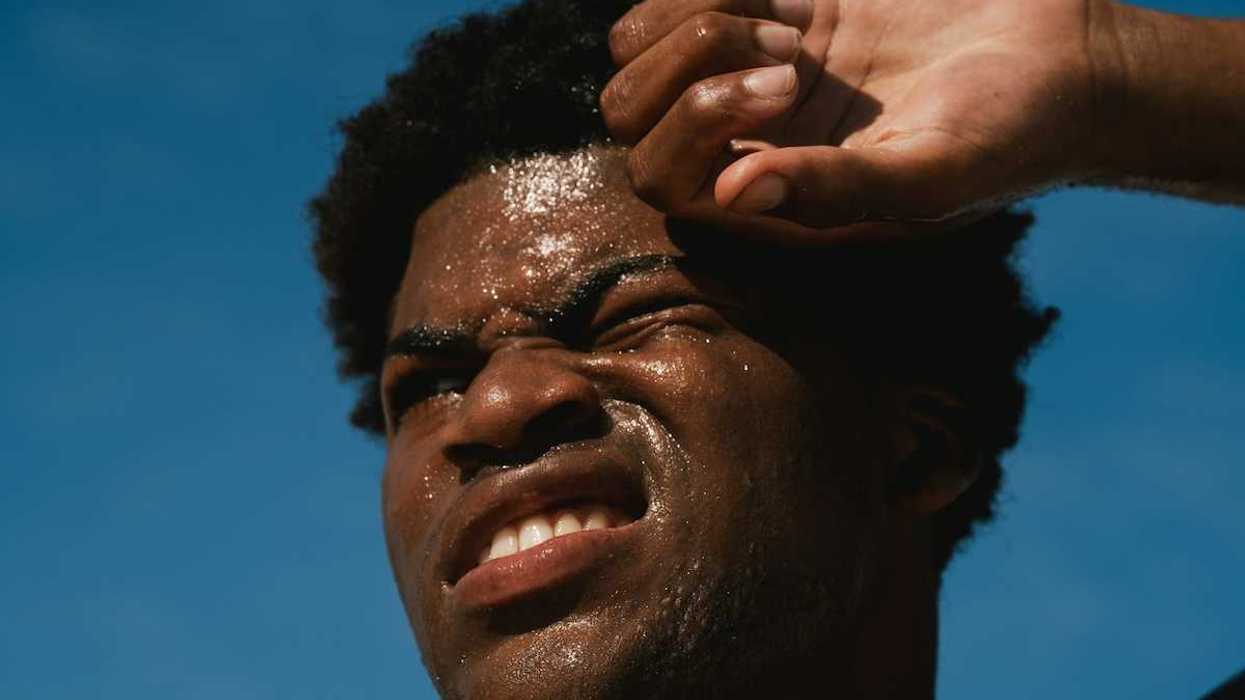 Head shot of Black man against blue sky with sweat-beaded face suffering from the heat