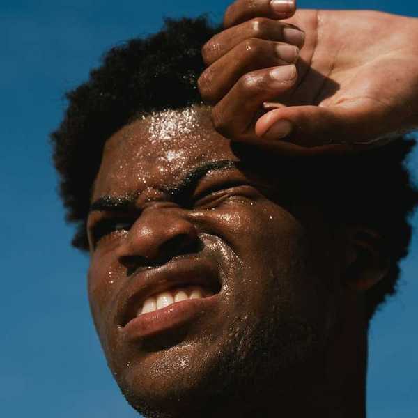 Head shot of Black man against blue sky with sweat-beaded face suffering from the heat