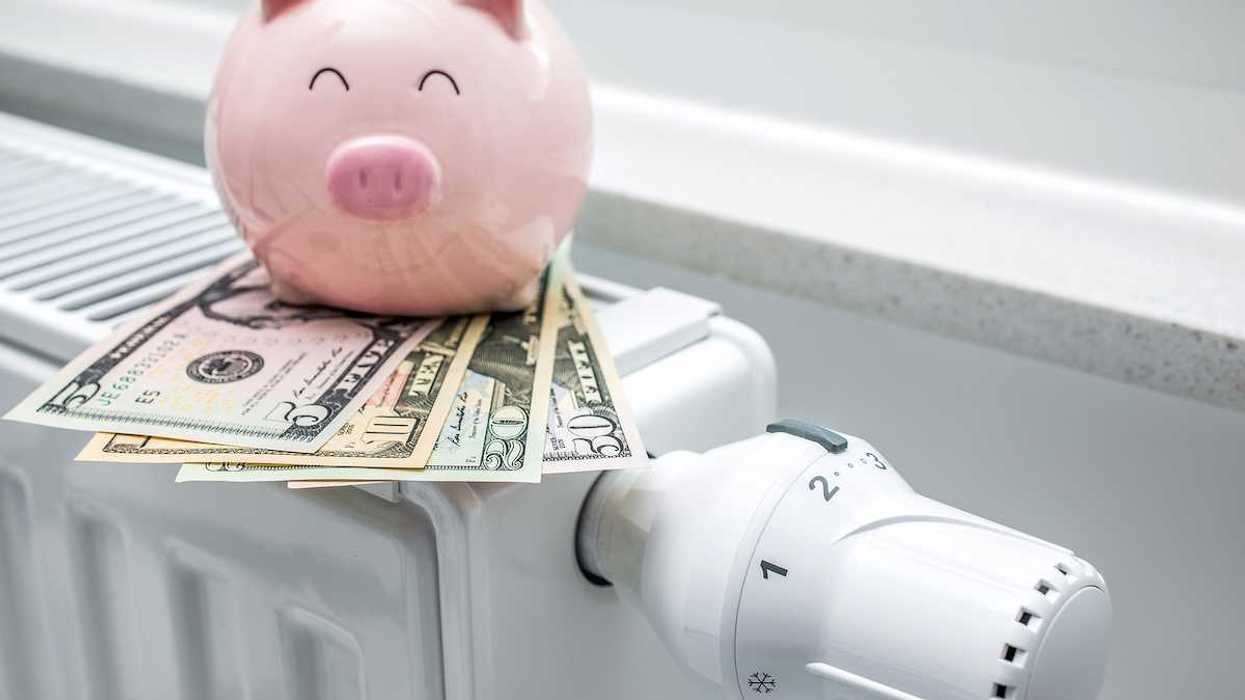 Heating thermostat on space heater with piggy bank and money indicating expensive heating costs