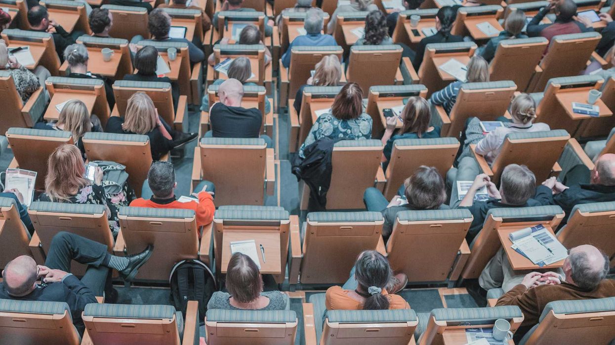 high-angle photography of group of people sitting at chairs in a conference auditorium.