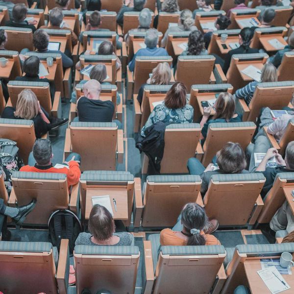 high-angle photography of group of people sitting at chairs in a conference auditorium.