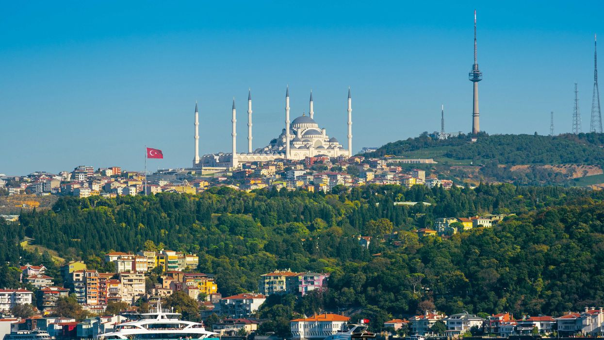 Image of a city in Turkey with ornate buildings on a hillside and a body of water in foreground.