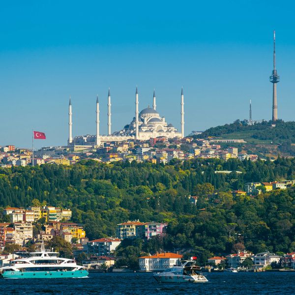 Image of a city in Turkey with ornate buildings on a hillside and a body of water in foreground.