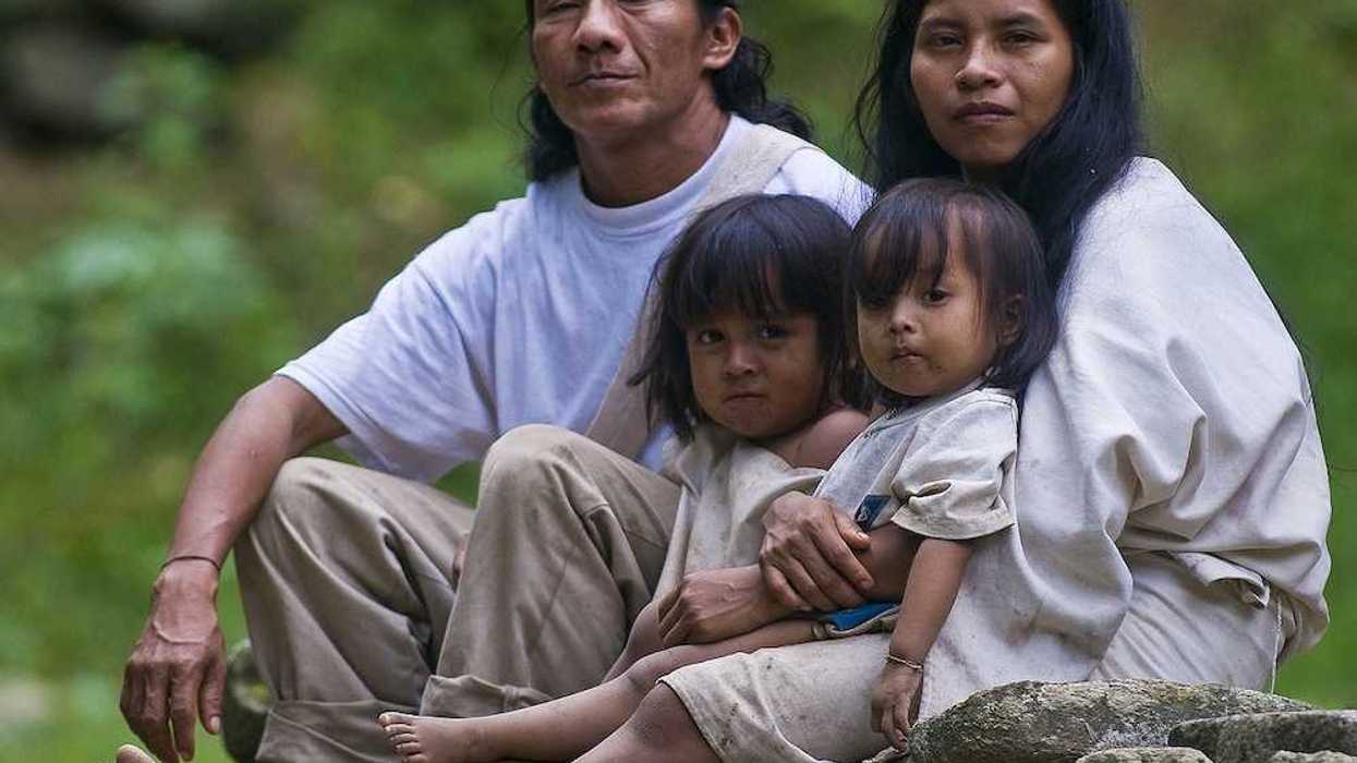 Indian family — man, woman, and two small girls — sit together at home in a village in "Tayrona" park Colombia