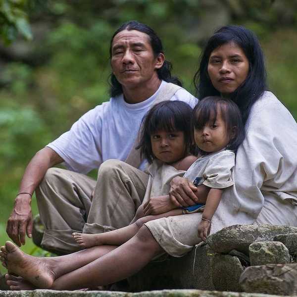 Indian family — man, woman, and two small girls — sit together at home in a village in "Tayrona" park Colombia