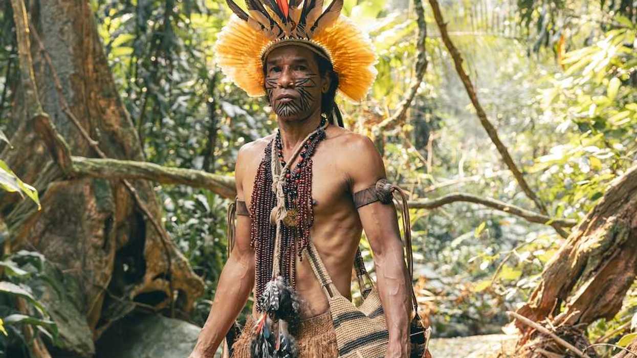 Indigenous Amazonian clothed in traditional dress, carrying traditional implements & weapons