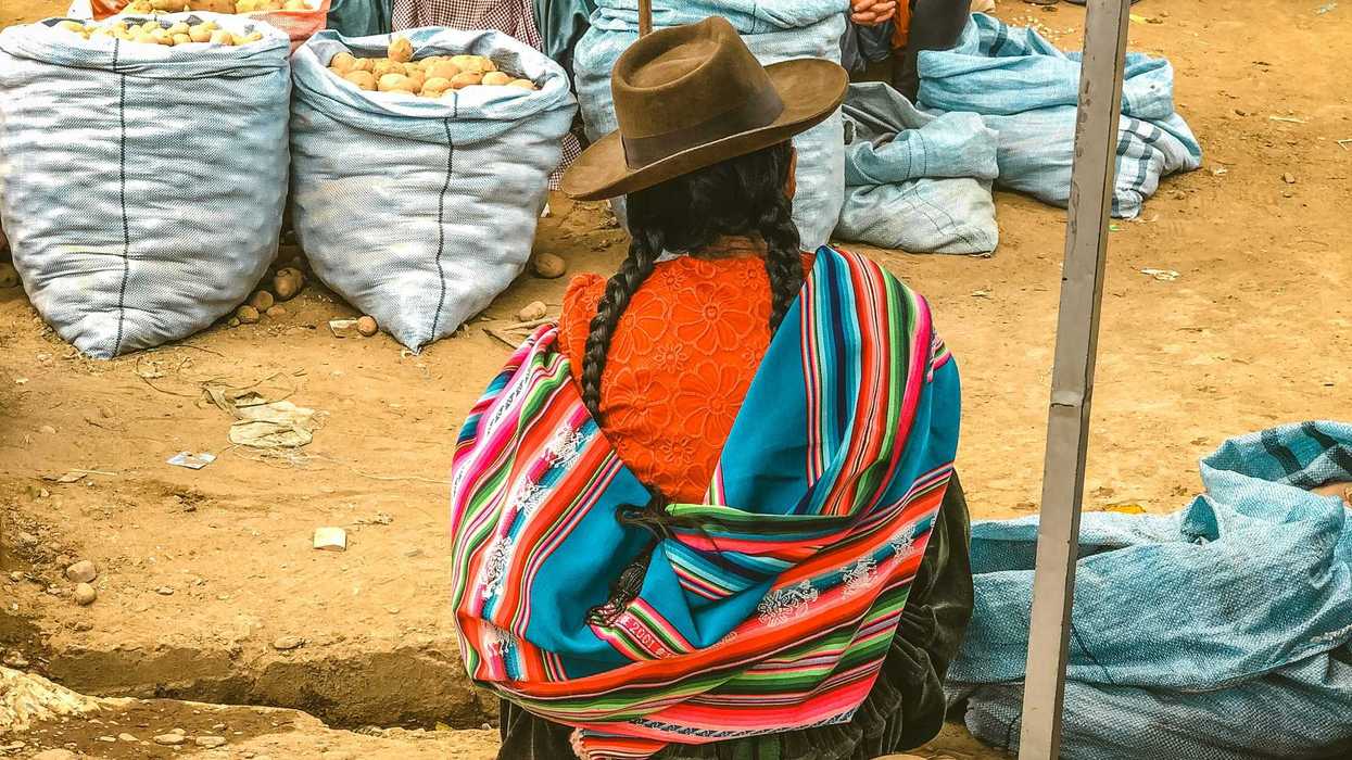 Indigenous women in colorful clothes sitting next to large bags of potatoes.
