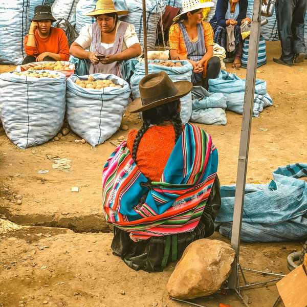 Indigenous women in colorful clothes sitting next to large bags of potatoes.