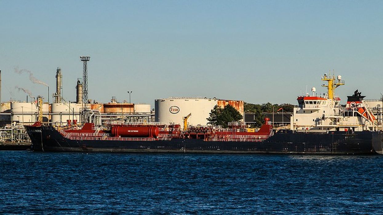 Industrial area with smokestacks and cargo ships on the water.