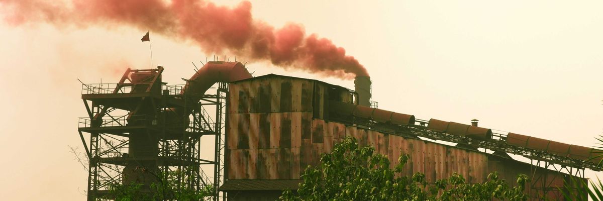 Industrial factory emitting red smoke against a hazy sky.