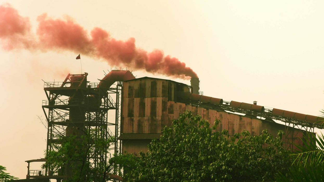 Industrial factory emitting red smoke against a hazy sky.