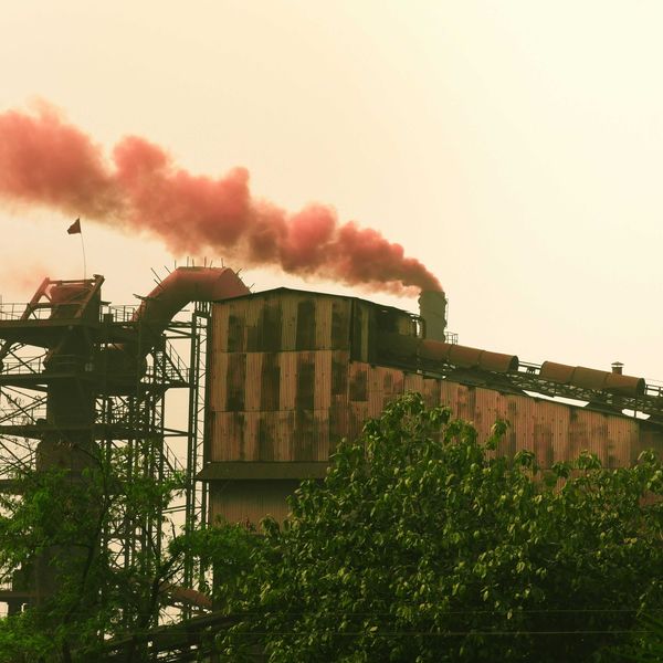 Industrial factory emitting red smoke against a hazy sky.