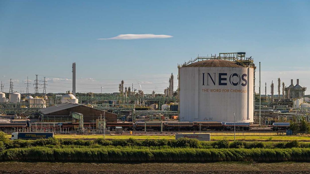 INEOS Zwijndrecht large storage tank with sign and slogan under blue sky. Green shoreline