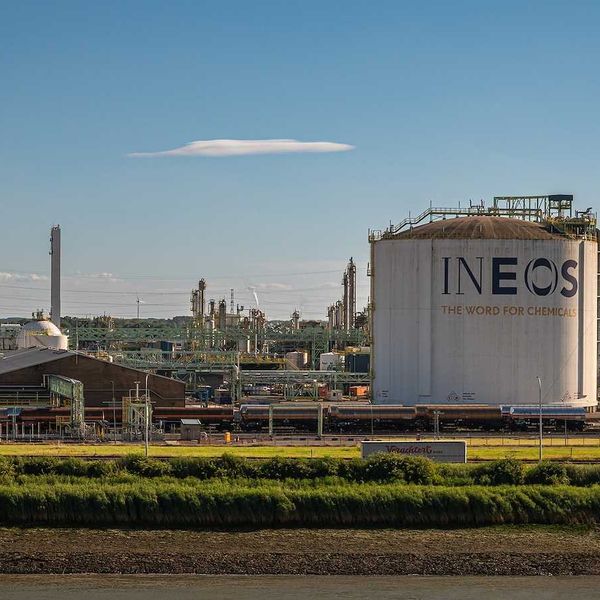 INEOS Zwijndrecht large storage tank with sign and slogan under blue sky. Green shoreline