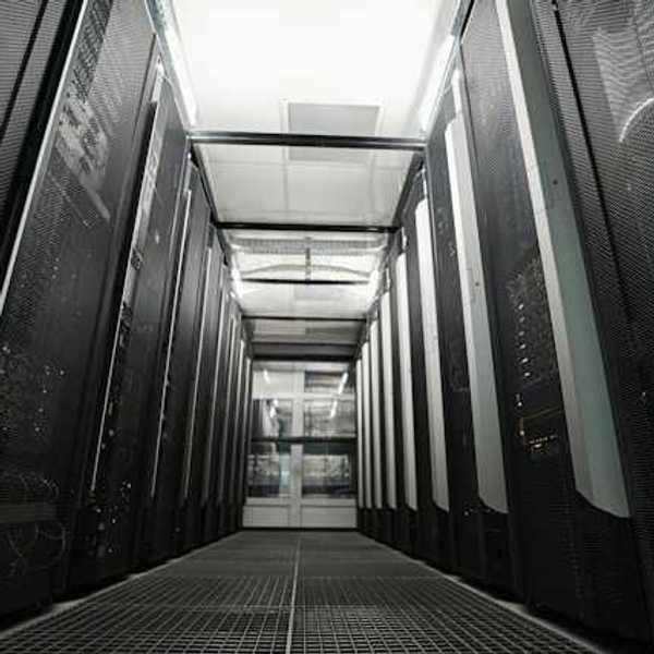Inside of a data center with black computers on either side of a pathway to walk through