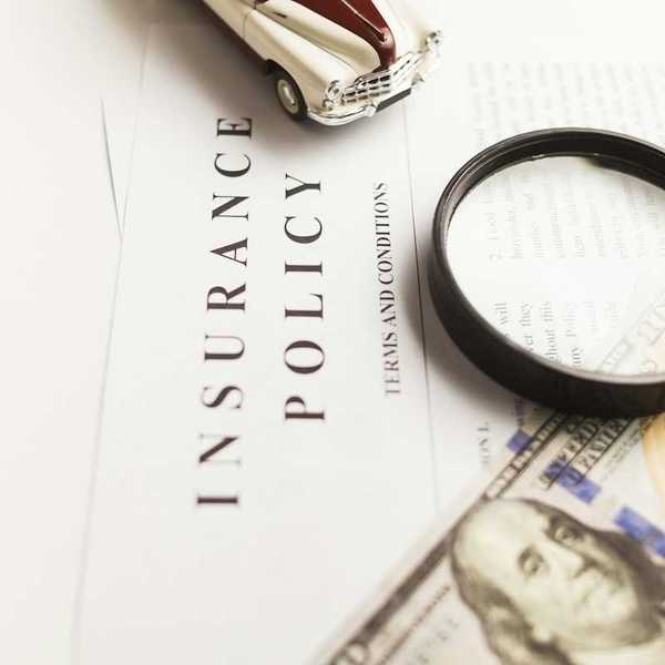 Insurance policy with magnifying glass, miniature auto, and hundred-dollar bill