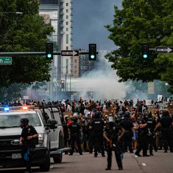 large crowd protesting with large police presence employing tear gas